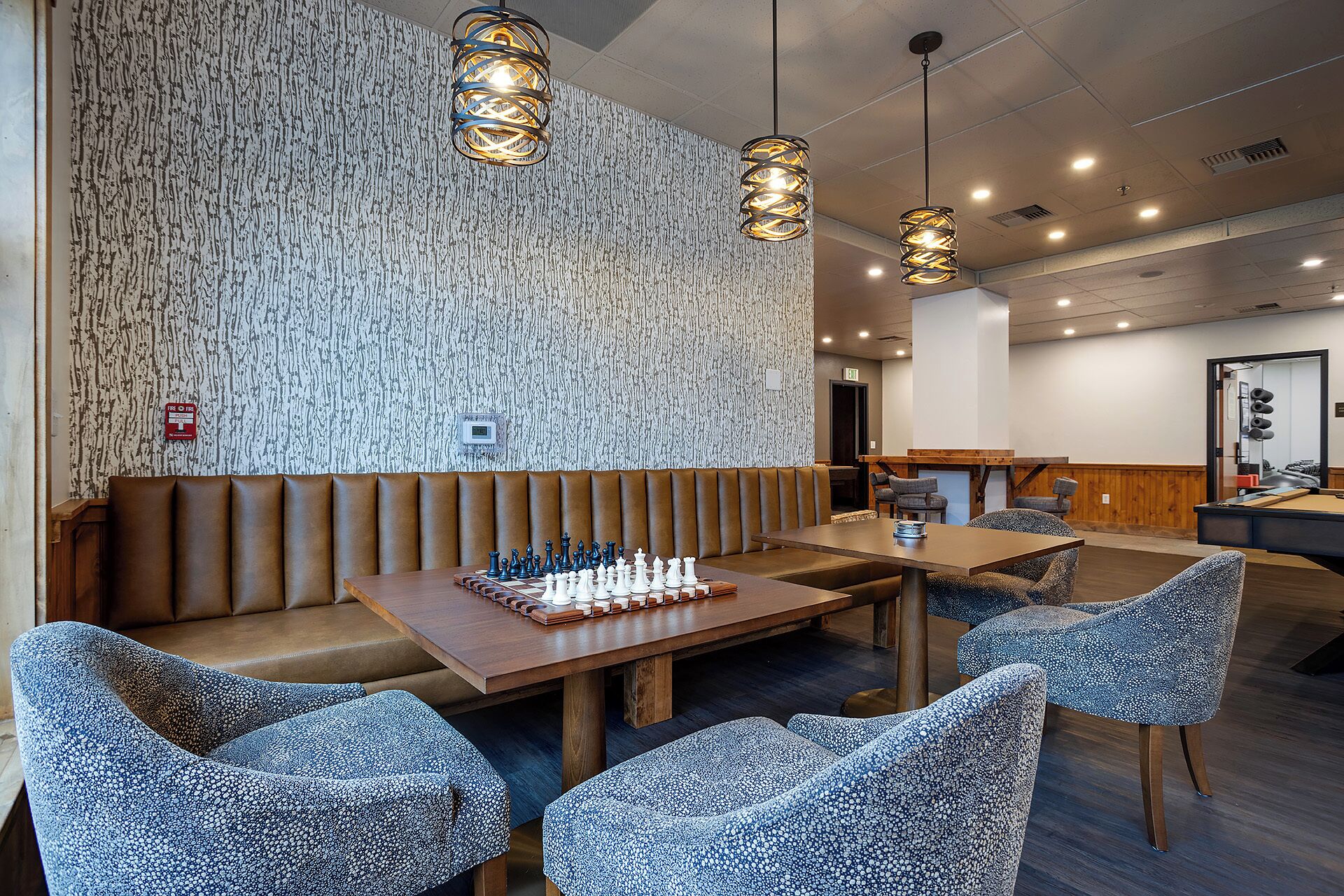 A modern dining area with a wooden table, chess set, and patterned chairs.