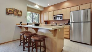 A modern kitchen with a central island, wooden cabinets, stainless steel appliances, and a large window providing natural light. - The Ridge at Sunriver - Condo #42 - Access provided to onsite seasonal swimming pool & tennis facilities, year-round hot tub plus 4 bikes (Sunriver)