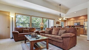 A spacious living room with a large brown leather sofa, a wooden coffee table, and a kitchen area with modern appliances. - The Ridge at Sunriver - Condo #42 - Access provided to onsite seasonal swimming pool & tennis facilities, year-round hot tub plus 4 bikes (Sunriver)