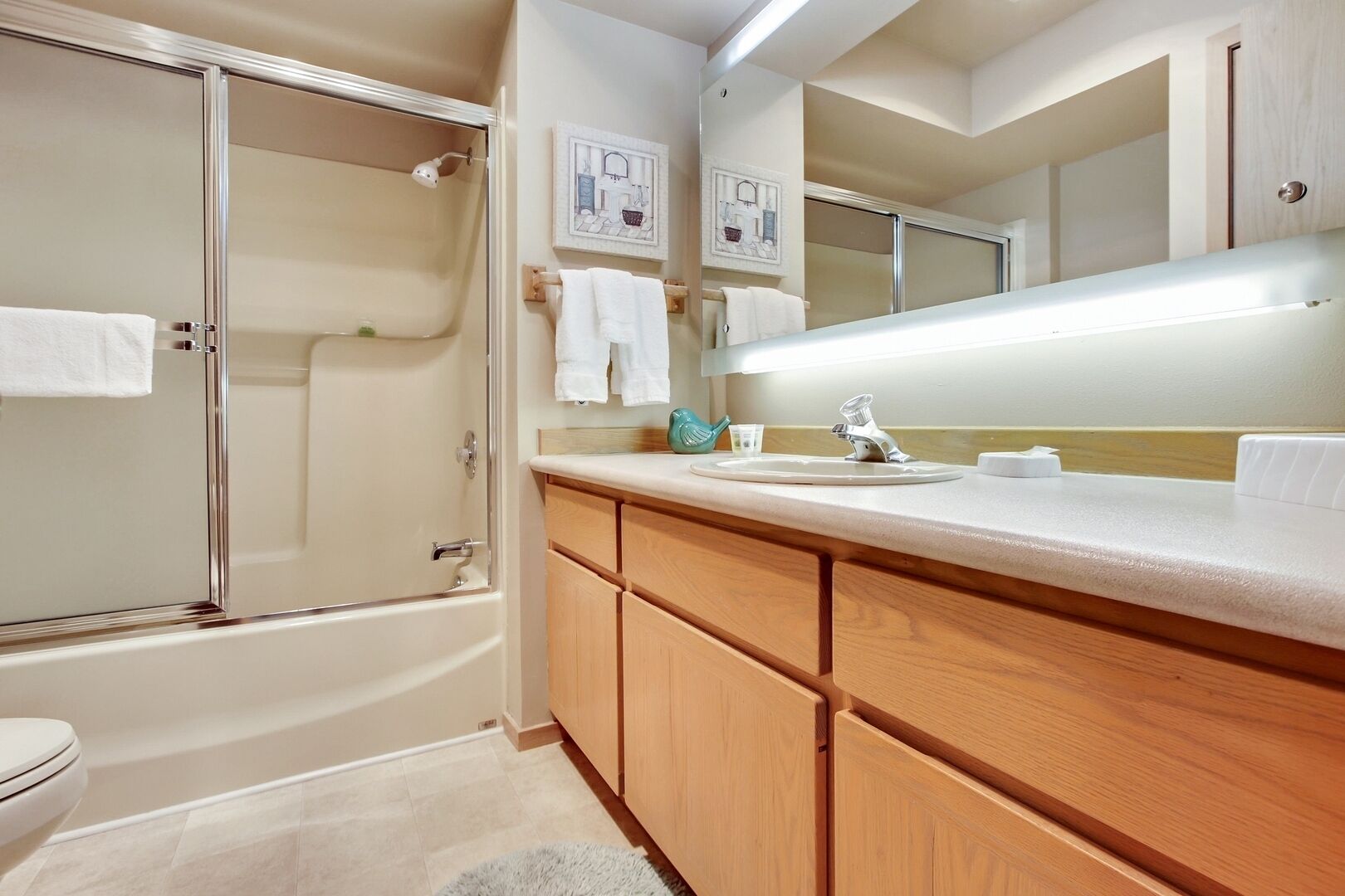 A modern bathroom with a glass-enclosed shower, wooden cabinets, a white sink, and a large mirror.