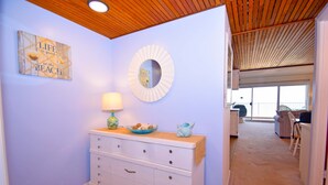 A room with a wooden ceiling, a white dresser with drawers, a round mirror, and a wall with a 'Life is good at the beach' sign. - Beachmark 3F-Oceanfront 73rd St, WIFI, Pool, Elev, W/D, AC (Ocean City)