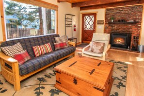 A cozy living room with a plaid sofa, a wooden coffee table, a fireplace, and a door with a welcome sign.