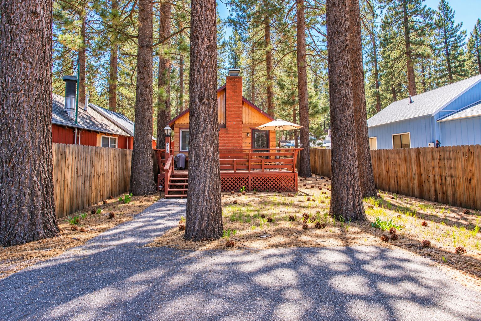 Une cabane entourée de grands arbres, dotée d’une terrasse en bois et d’un espace extérieur aménagé et abrité.