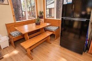 A compact kitchen with a wooden table, bench seating, a black refrigerator, and a window with a view of a wooden deck.