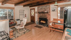 Una sala de estar acogedora con chimenea, vigas de madera, un sofá, una silla y una mesa de comedor.