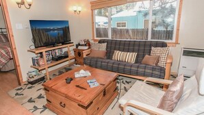 Una sala de estar acogedora con un sofá, una mesa de centro de madera, un televisor y una estantería.