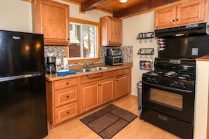 A kitchen with wooden cabinets, a black refrigerator, a microwave, a stove, and a sink.