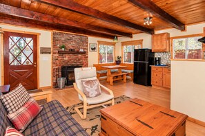 A cozy cabin interior with a fireplace, wooden furniture, and a kitchen area.
