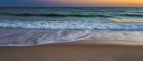 A beach with waves, a clear sky, and a sunset.