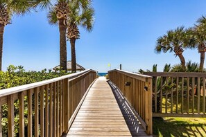A wooden boardwalk leading to a beach with palm trees and a clear sky.