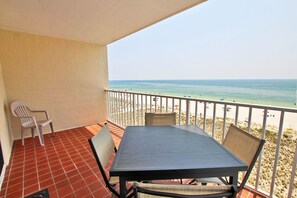 Un balcón con mesa y sillas, con vista a una playa con gente y sombrillas.