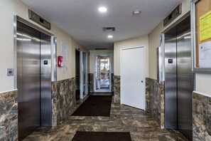 A hallway with two elevators, marble flooring, and a door at the end.
