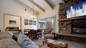 A cozy living room with a stone fireplace, a sofa set, a dining area, and a large window. - SE064 | Great Ski Access | Winter Shuttle | Hot Tub (Steamboat Springs)