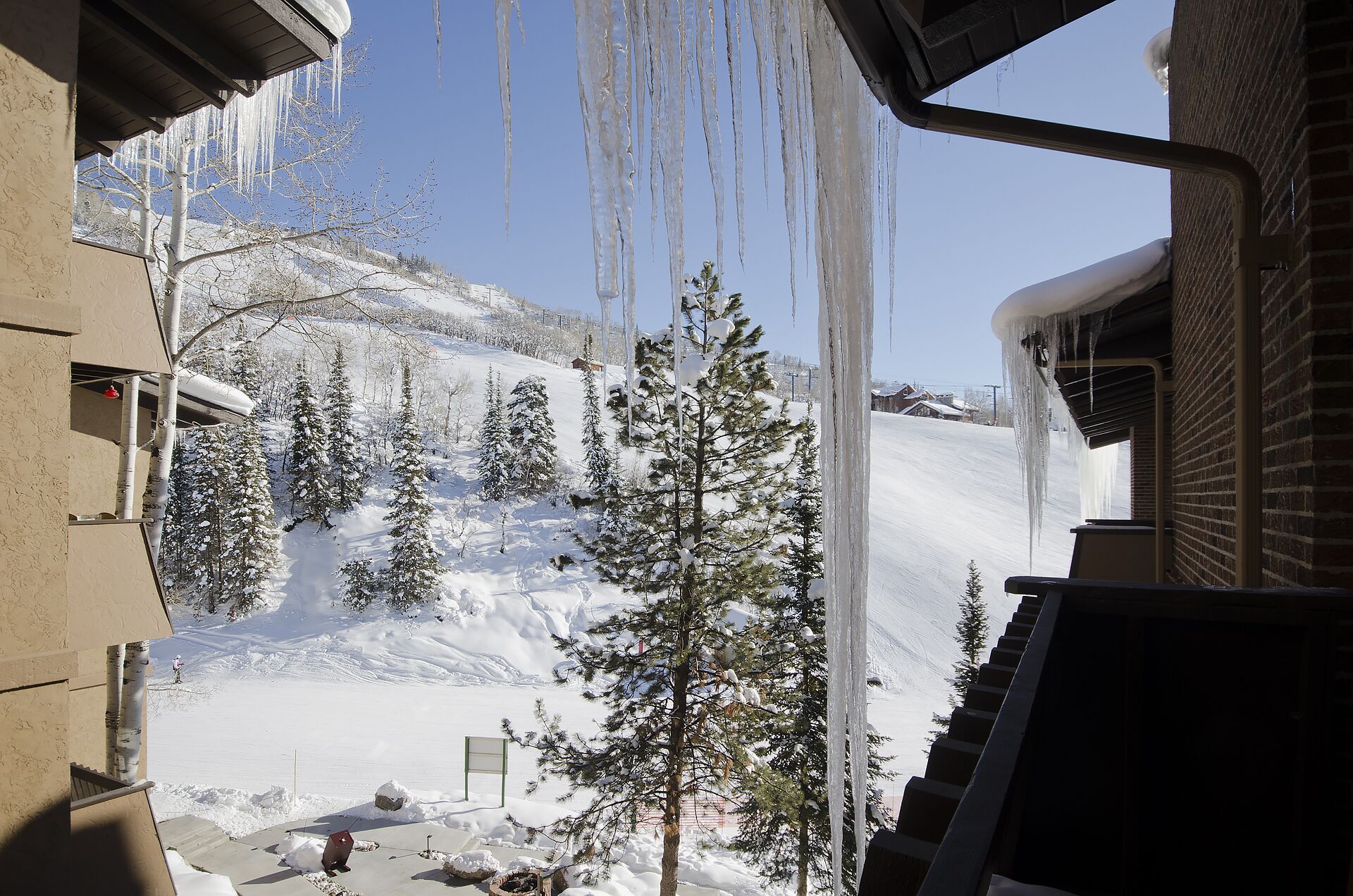 A snowy landscape with icicles hanging from a building's roof, a snow-covered slope, and evergreen trees.