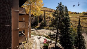 A building with a brick facade, a paved area with outdoor seating, and a view of a hillside with trees and a cable car in the background. - SE064 | Great Ski Access | Winter Shuttle | Hot Tub (Steamboat Springs)