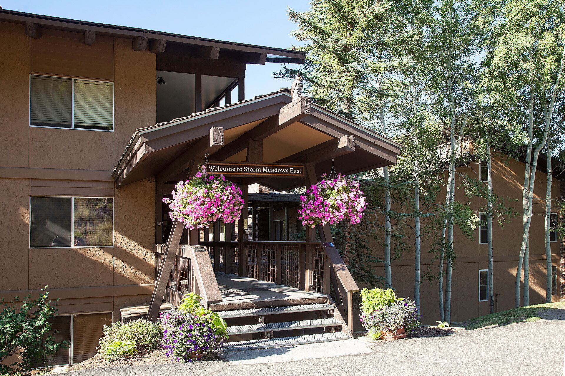 Un bâtiment doté d’un porche en bois, d’une enseigne indiquant « Bienvenue à Storm Meadows East » et de jardinières suspendues.