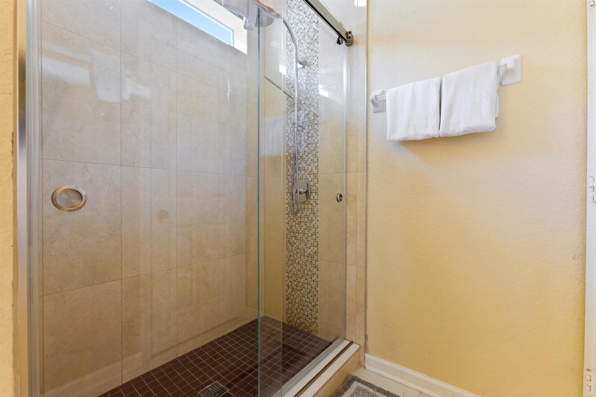 A glass-enclosed shower with a tiled floor and a small step leading up to it.