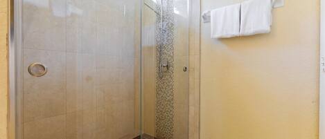 A glass-enclosed shower with a tiled floor and a small step leading up to it.