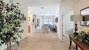 A spacious living area with a large plant, a sofa, a coffee table, and a dining area in the background.