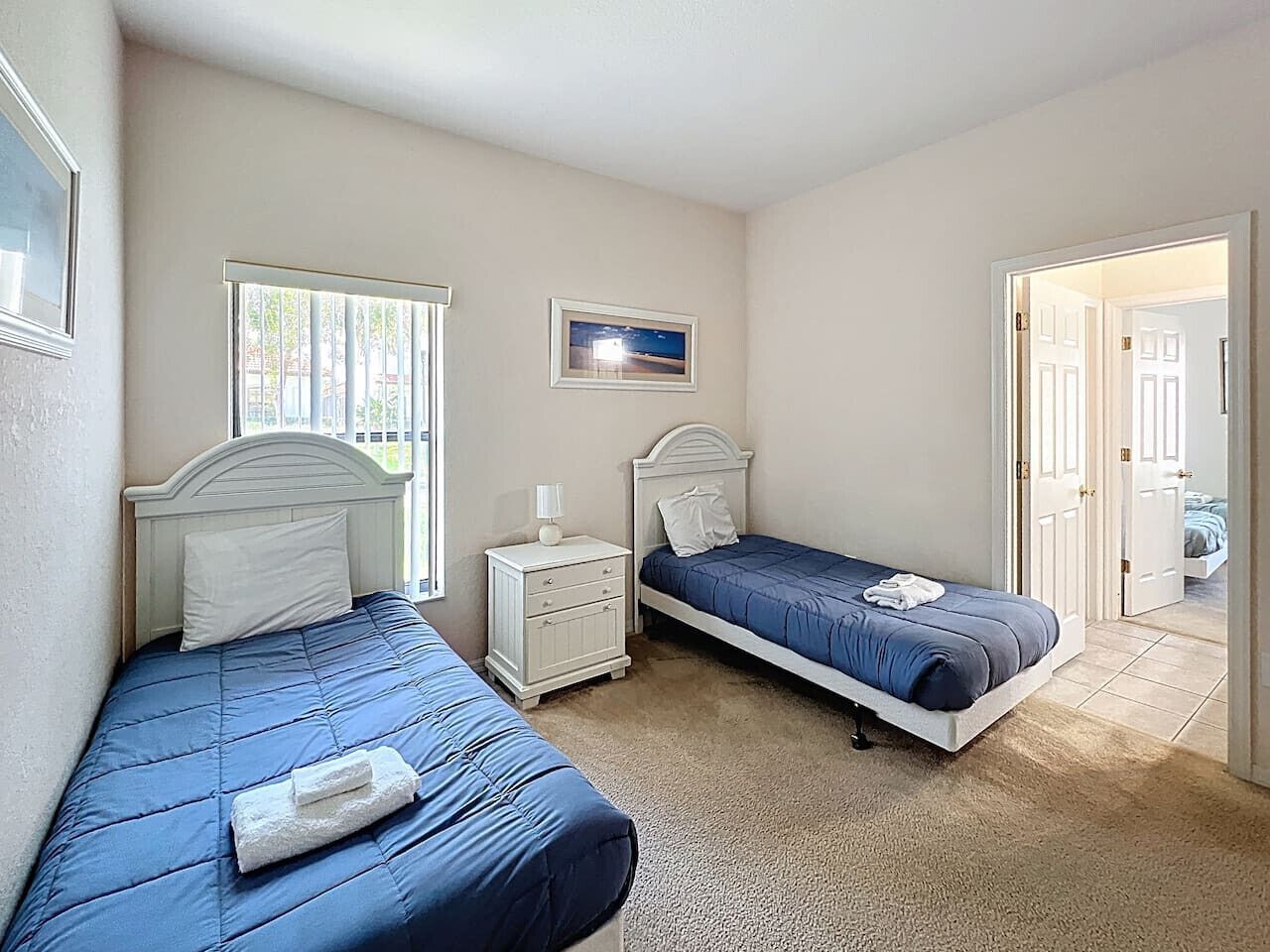 A bedroom with two beds, a nightstand, and a window.