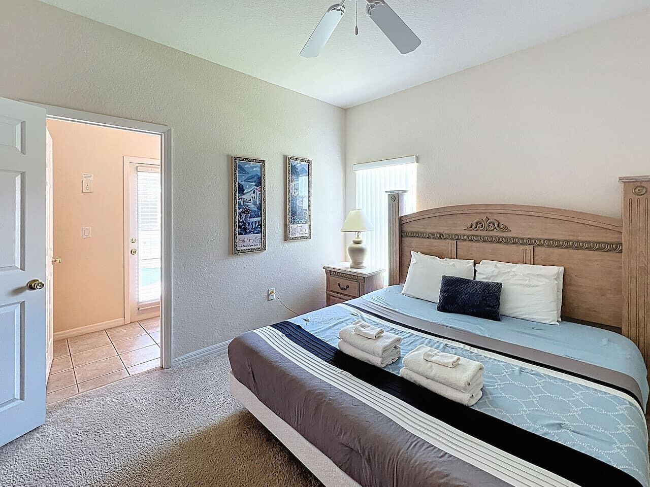 A bedroom with a bed, bedside table, lamp, and wall art.