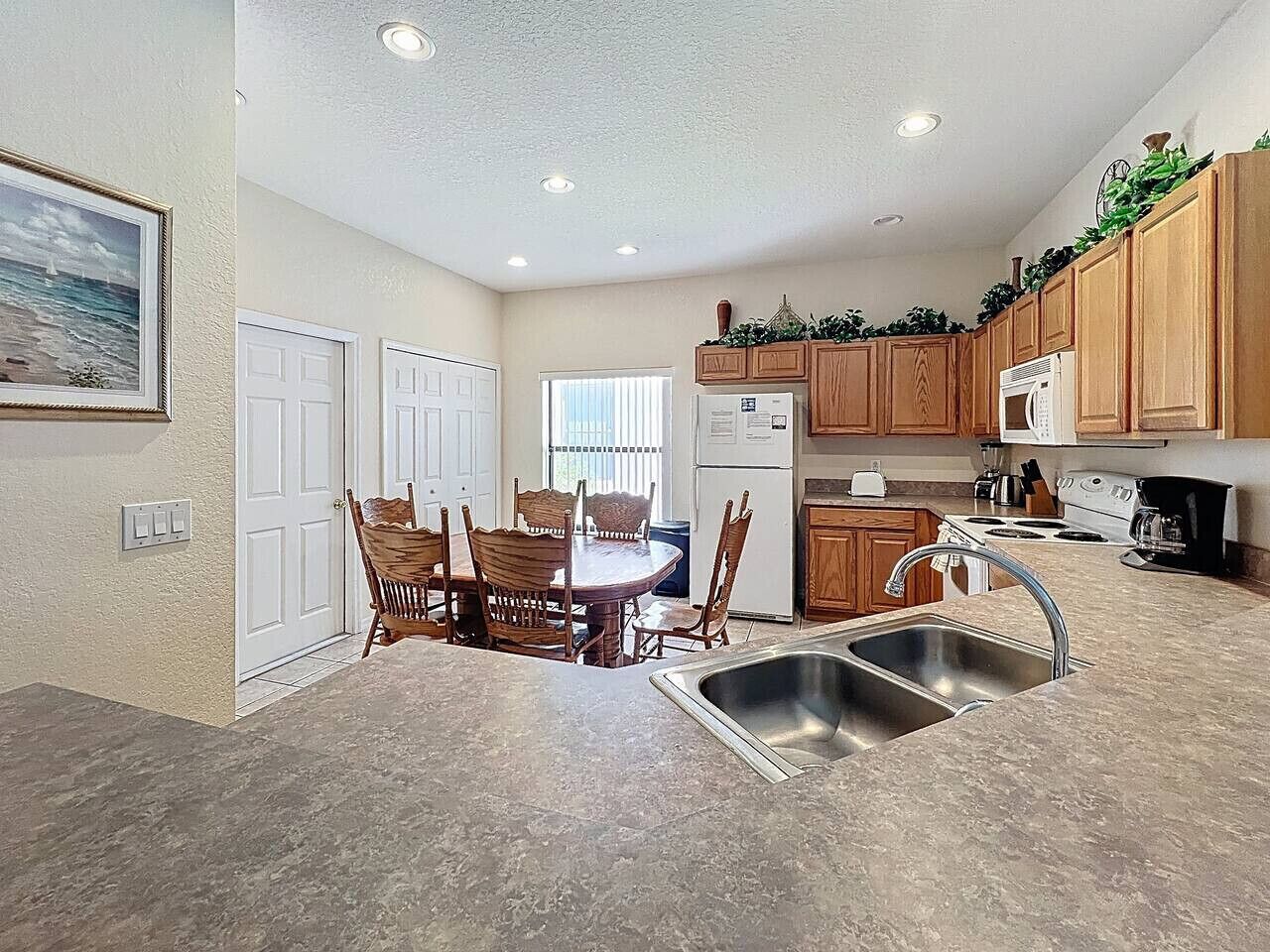 A compact kitchen with wooden cabinets, a dining table with chairs, a refrigerator, a stove, and a sink.