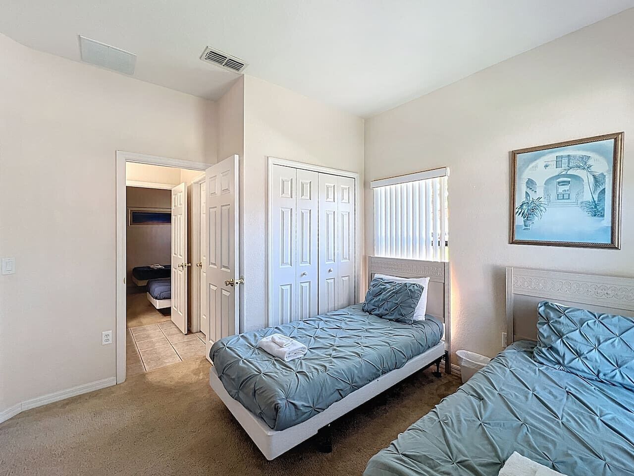 A bedroom with two single beds, a door leading to a bathroom, and a framed picture on the wall.