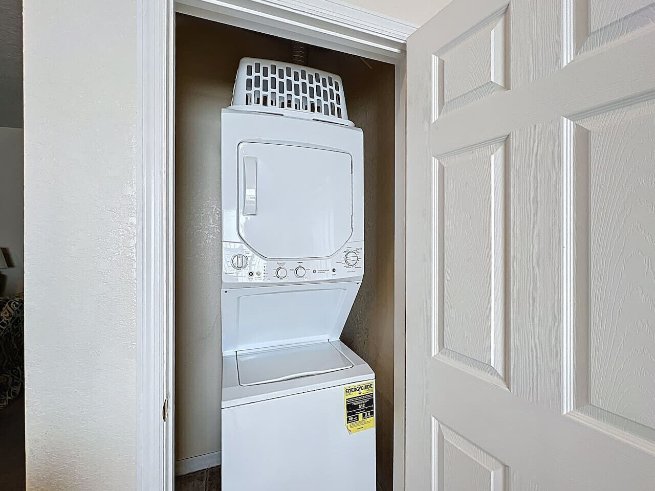 A compact washer and dryer unit in a narrow hallway with a door on one side.