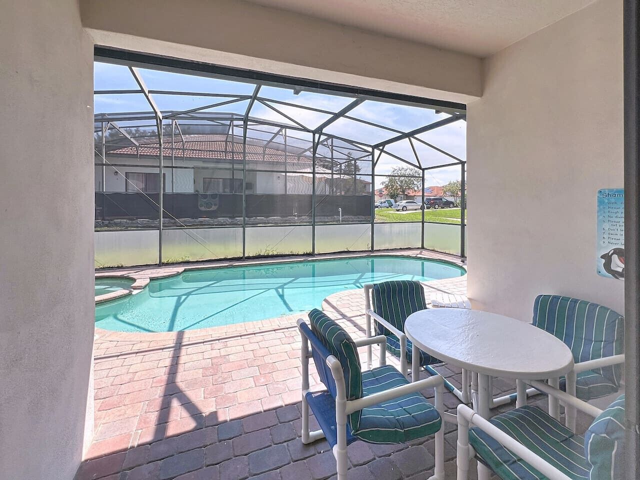 A covered patio with a pool, outdoor seating, and a view of a residential area.