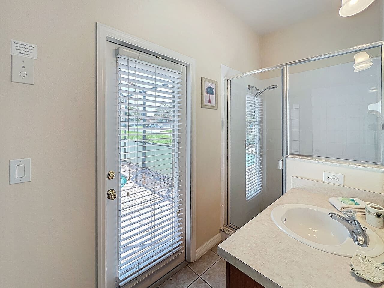 A bathroom with a sink, mirror, and a door with blinds.