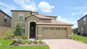 A two-story house with a beige facade, a red-tiled roof, and a garage. - Championsgate Resort 6 Bedroom Pool Home with Game Room (Davenport)