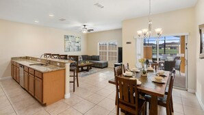 A spacious kitchen with a granite countertop and wooden cabinets, a dining area with a chandelier, and a view of a lake through large windows. - Paradise Palms Resort 4 Bedroom Townhome Pet Friendly (Kissimmee)