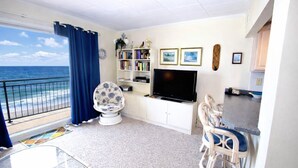 Uma sala de estar com vista para o oceano, uma televisão, uma estante de livros e um espaço para refeições.
