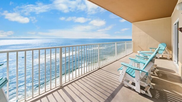A balcony with a view of the ocean, equipped with white railings and turquoise chairs.