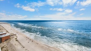 A beach with a building on the left, waves crashing onto the shore, and a clear sky.