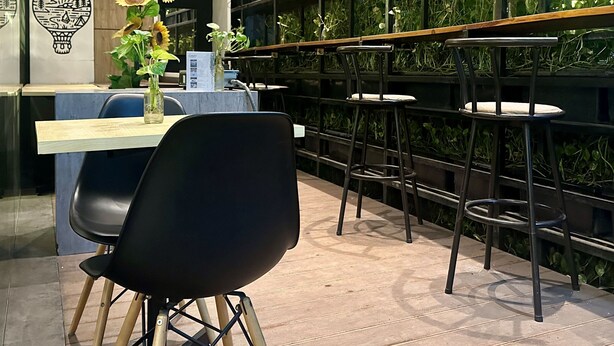 A modern bar area with a black chair, a wooden table, and a wall with greenery. - Sunrise Hotel Semarang (Semarang)