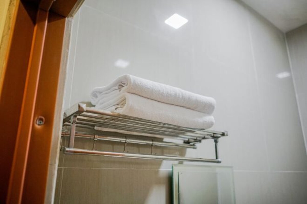 A bathroom with a towel rack holding folded towels, a mirror, and a shower area.