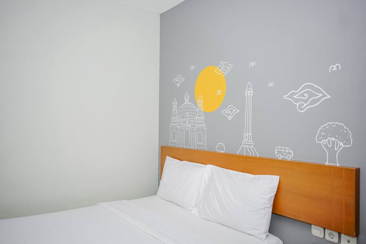 A hotel room with a bed, a wooden headboard, and a wall with travel-themed drawings.