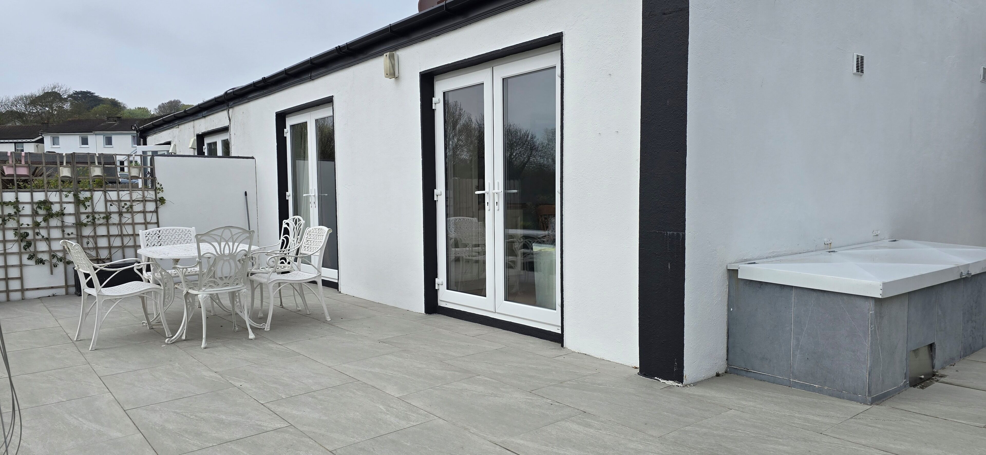 A patio area with a table and chairs, a white wall, and a sliding glass door.