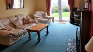 A living room with a beige sofa, a wooden coffee table, a television on a stand, and a large window with curtains.