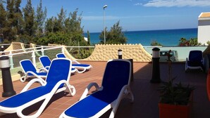 Une terrasse sur le toit, avec des fauteuils bleus, un pot de fleurs et une vue sur la mer.