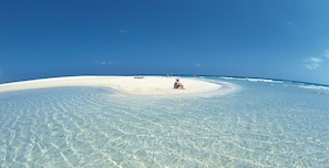 Ein Strand mit klarem türkisblauem Wasser, einem Sandstrand und einigen Personen.