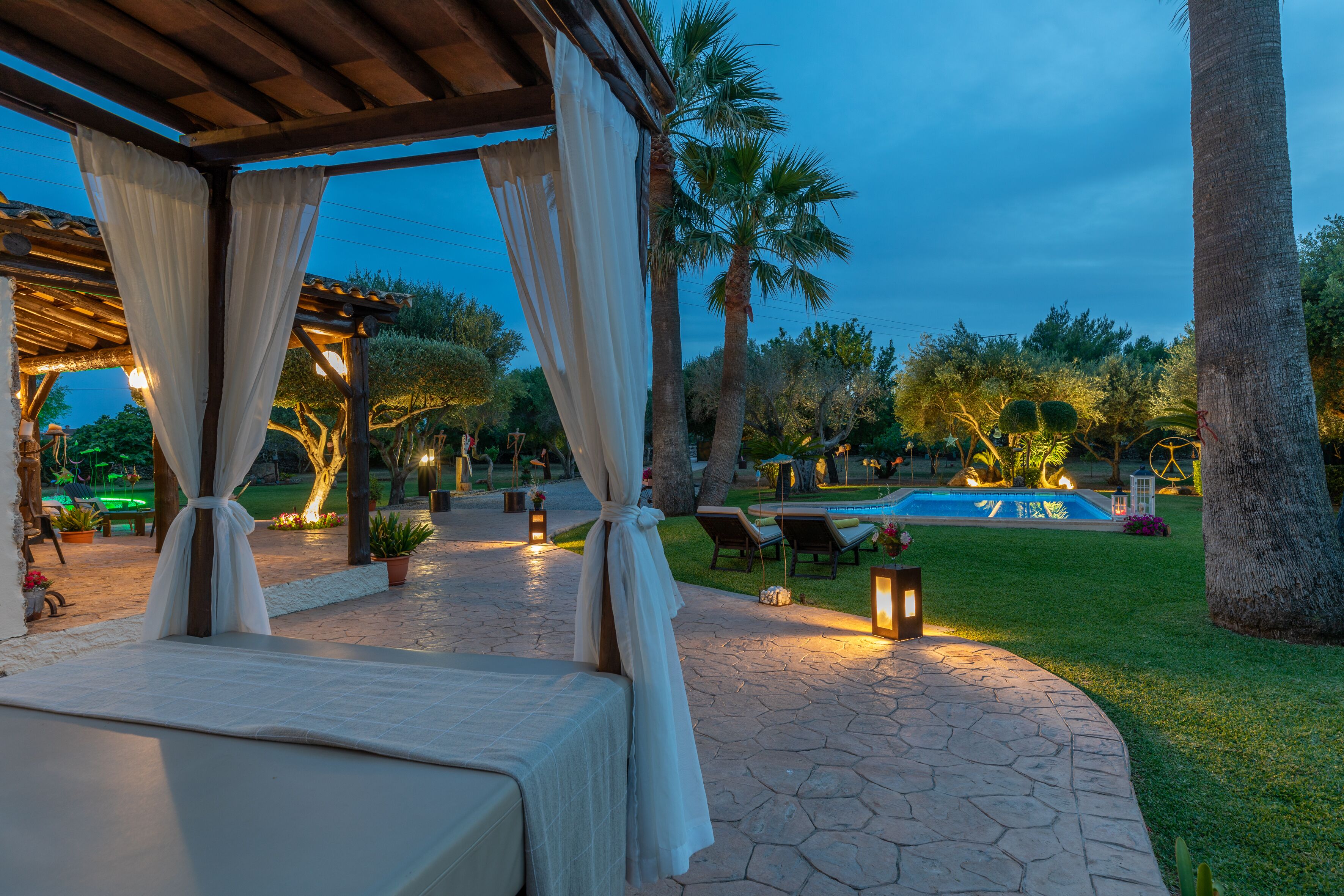 A covered outdoor seating area with a pool and palm trees in the background.