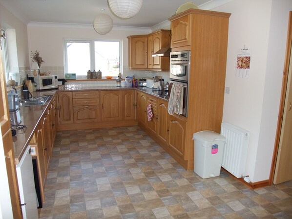 A kitchen with wooden cabinets, a microwave, an oven, and a sink. - Magnificent views from our 2 Bedroom well appointed, comfortable family home (Northton)