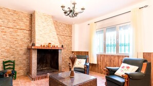 A living room with a fireplace, a chandelier, a sofa, and a window with curtains. - Cottage with pool, garden with views and wifi (Dúrcal)