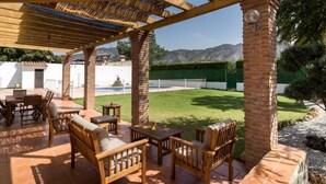 An outdoor patio with wooden furniture and a pergola, overlooking a well-maintained lawn and mountains. - Cottage with pool, garden with views and wifi (Dúrcal)