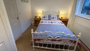 A bedroom with a bed, bedside lamps, a radiator, and a window.