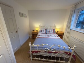 A bedroom with a bed, bedside lamps, a radiator, and a window.