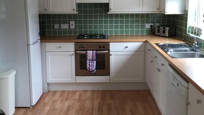A kitchen with white cabinets, a green tiled backsplash, a wooden countertop, a stove, a dishwasher, and a window with a view. - Mountfield - For families, walkers and cyclists (Freshwater)