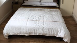 A bedroom with a sloped ceiling, a bed with white bedding, a nightstand with a lamp, and wooden flooring. - Mountfield - For families, walkers and cyclists (Freshwater)